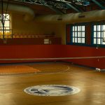 Spacious gym with volleyball net and basketball hoop, ideal for sports activities.