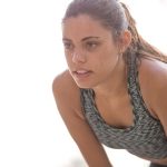 Active woman in workout attire taking a break during exercise outdoors.